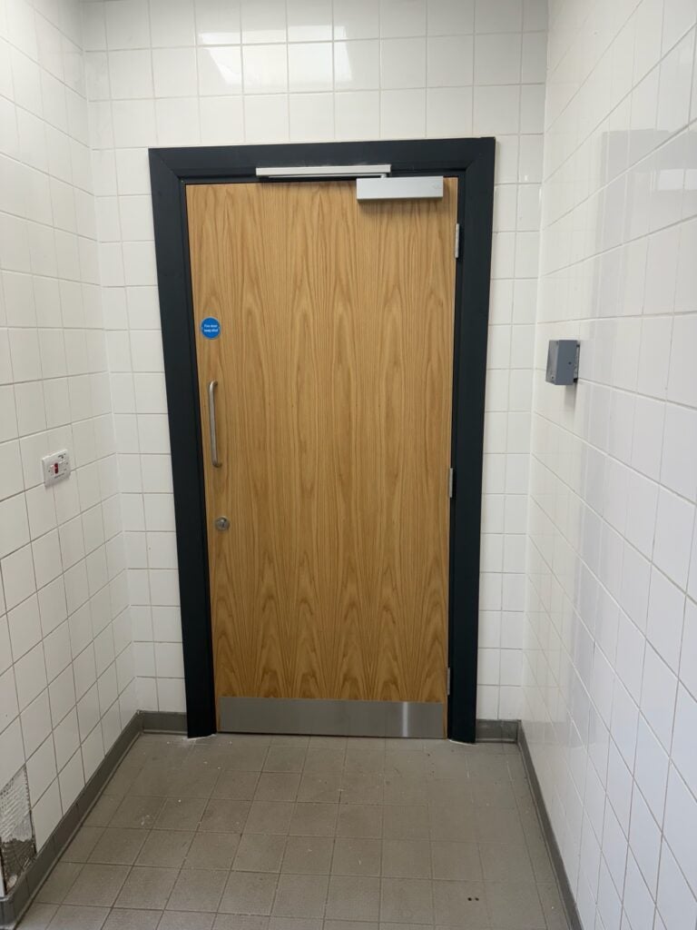 Installed wooden fire door with door closer and keep shut sign in UK corridor